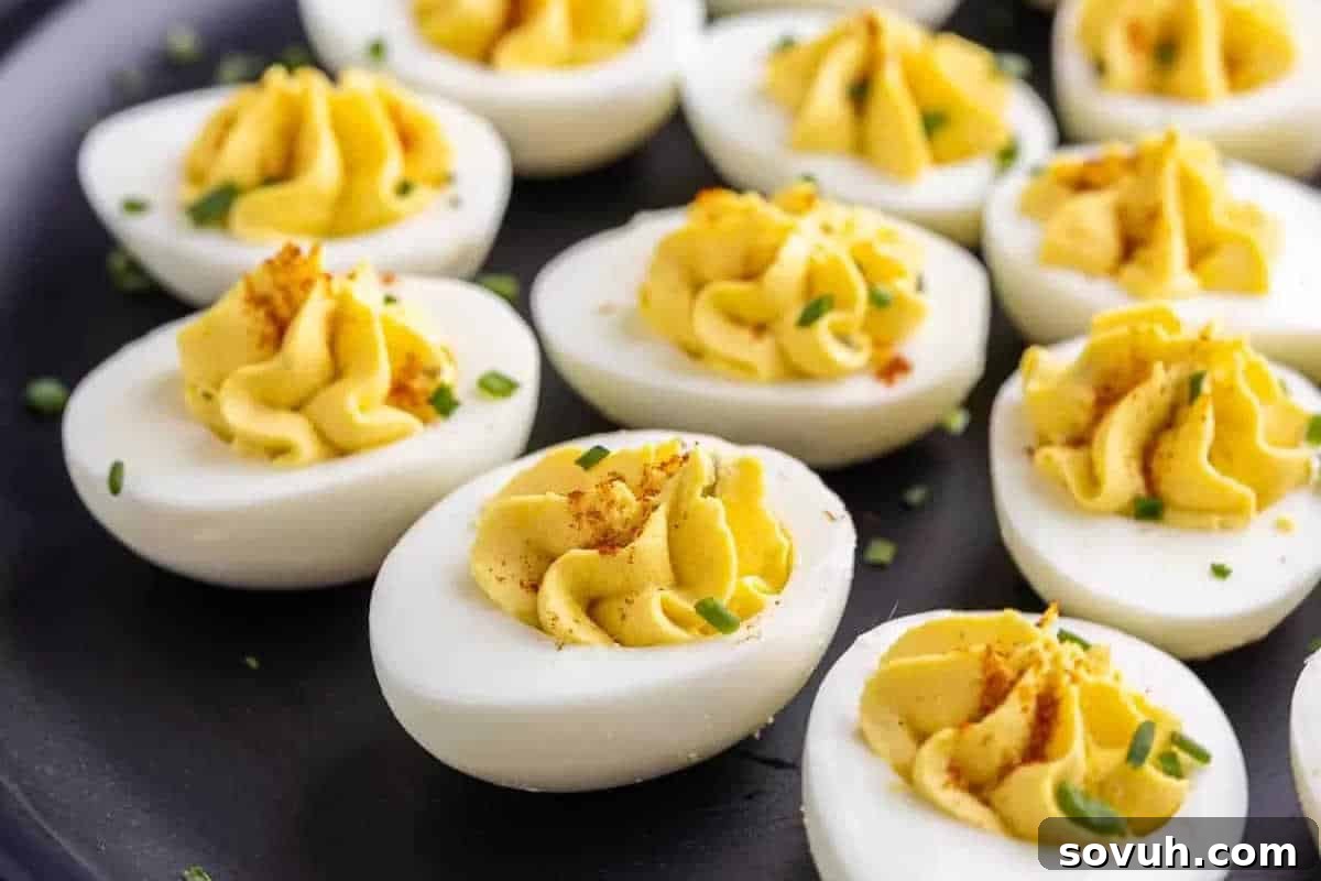 A plate of deviled eggs garnished with paprika and chopped chives. Each half is filled with a smooth, yellow filling.