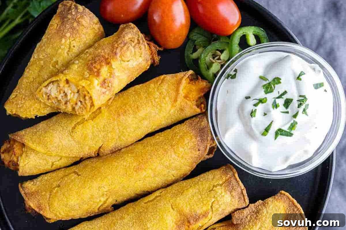 A plate of crispy taquitos with a side of sliced jalapeños, cherry tomatoes, and a small glass bowl of sour cream topped with chopped chives.