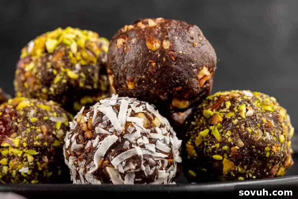 A close-up of several chocolate energy bites, some coated with nuts and one with shredded coconut, arranged on a black plate.