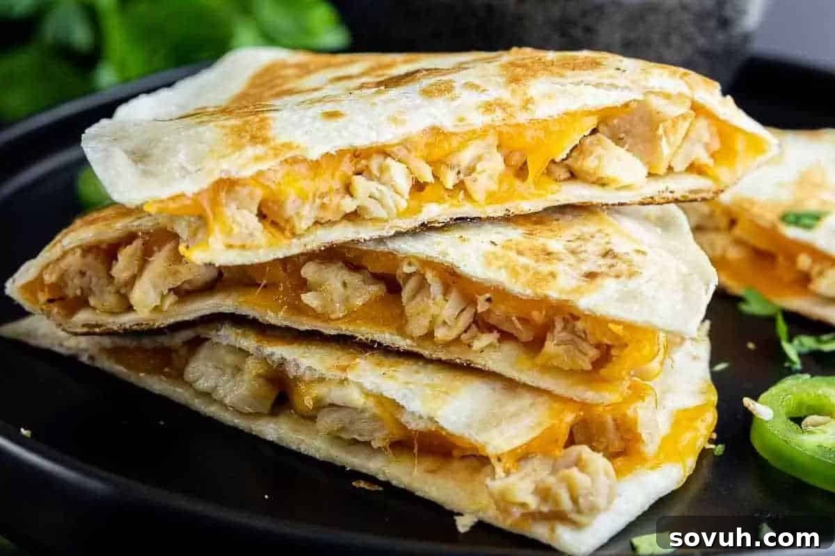 Three stacked chicken quesadilla slices with melted cheese and grilled tortillas on a dark plate.