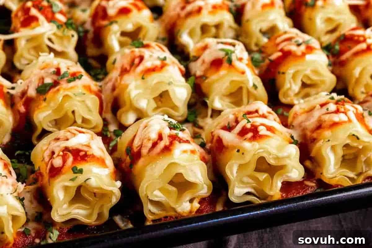 A baking tray filled with rolled pasta topped with tomato sauce, melted cheese, and garnished with chopped herbs.