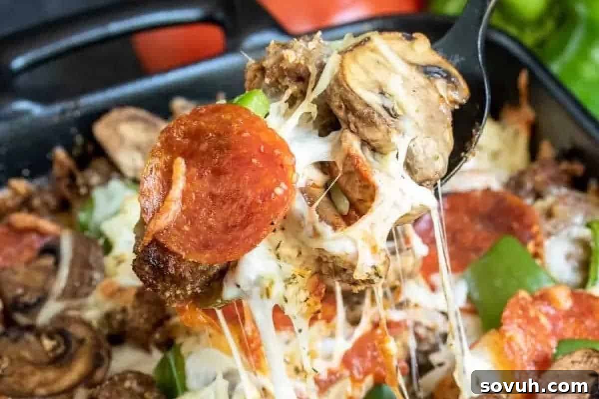 Close-up of a spoon lifting a generous slice of golden, cheesy pizza bake, revealing delectable toppings including mushrooms, pepperoni, and vibrant green bell peppers, all without the carbs.