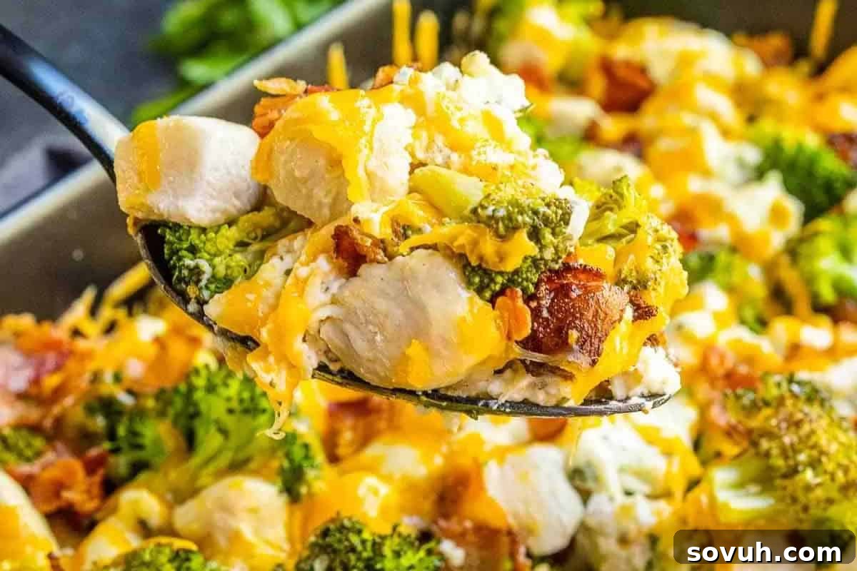 A spoonful of Keto Chicken Bacon Ranch Casserole, topped with melted cheese and crispy bacon, held above a baking dish with more of the delicious dish in the background.