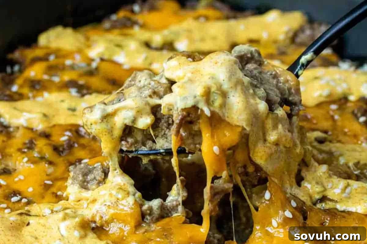 Close-up of a serving of cheesy ground beef casserole, adorned with sesame seeds and showcasing delicious melted cheese being effortlessly lifted by a spoon, reminiscent of a Big Mac.
