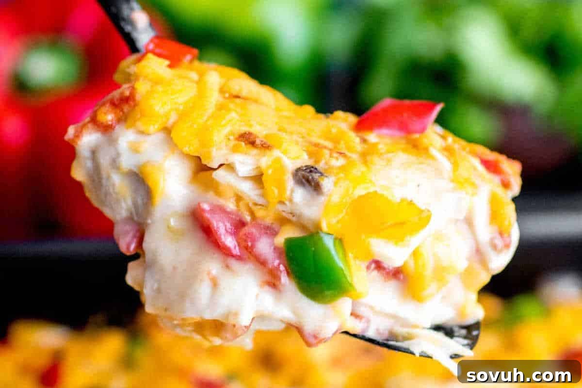 A close-up of a serving of cheesy King Ranch Chicken Casserole being lifted with a spatula, revealing layers of creamy chicken, melted cheese, and visible chunks of red and green bell peppers.