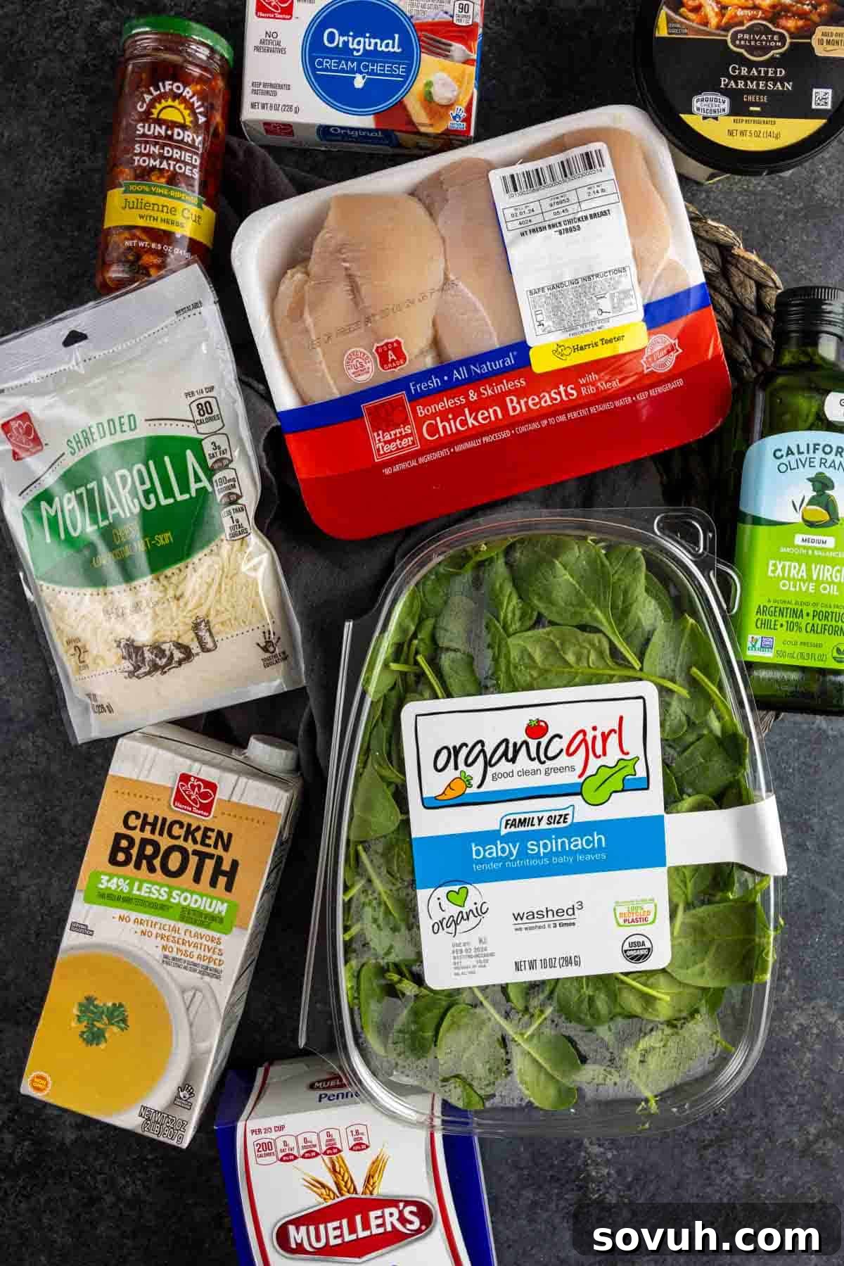 Carefully arranged ingredients for Chicken Florentine Pasta, including fresh chicken breasts, vibrant baby spinach, an assortment of cheeses, and sun-dried tomatoes, on a dark rustic surface.