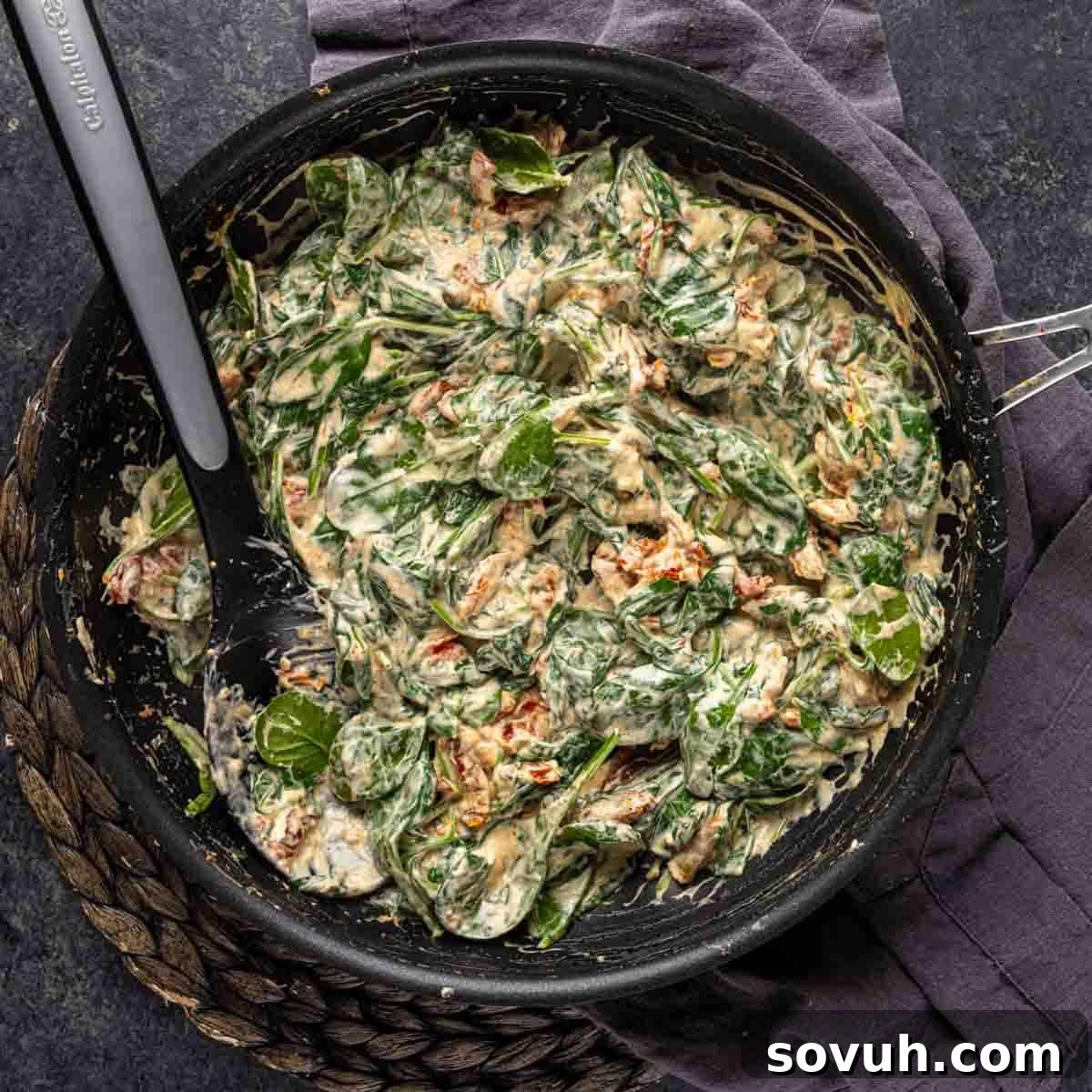 A close-up view of the rich, creamy Chicken Florentine sauce, featuring vibrant wilted spinach and pieces of melted cream cheese, simmering gently in a black skillet.