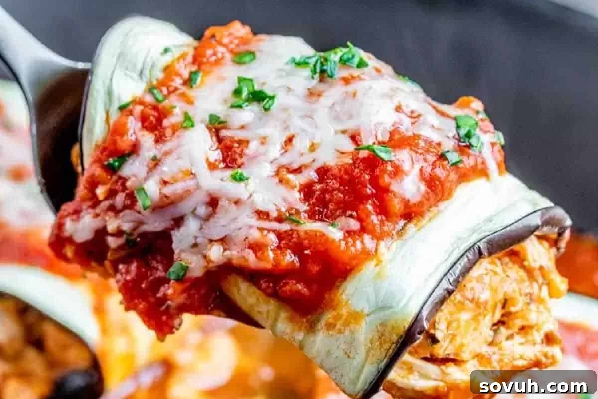 A close-up of a slice of eggplant parmesan being lifted by a spatula. The slice is covered in tomato sauce, melted cheese, and garnished with chopped herbs.