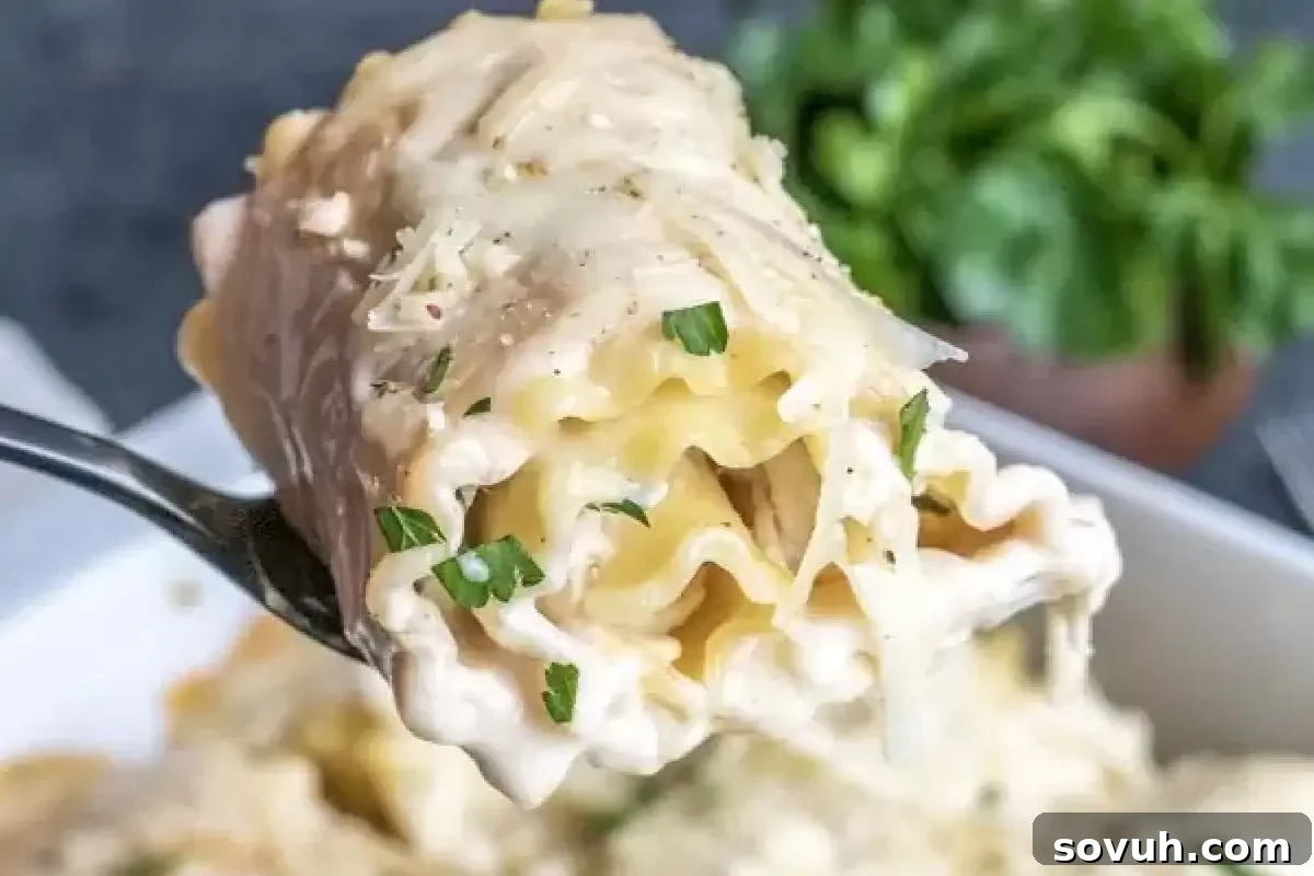 Close-up of a fork holding a piece of creamy, cheesy lasagna roll-up garnished with parsley, with a dish of more lasagna roll-ups and greens in the background.