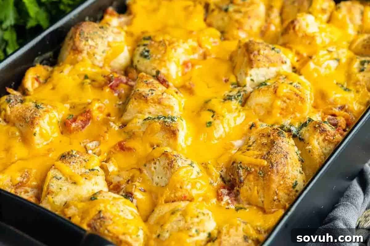 A close-up of a baked dish with chunks of bread, melted cheese, and garnished herbs in a black baking tray.