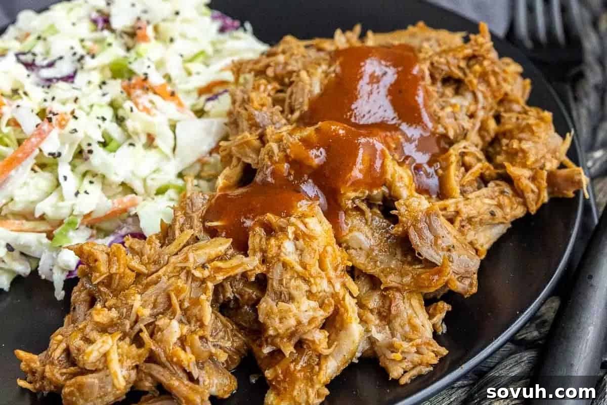 A generous serving of barbecue pulled pork, richly coated in sauce, accompanied by a side of fresh, creamy coleslaw on a plate.