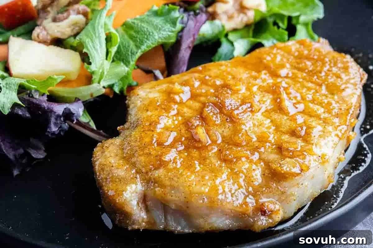 A glistening, cooked pork chop coated in a rich honey garlic sauce, served alongside a vibrant mix of fresh greens and vegetables.