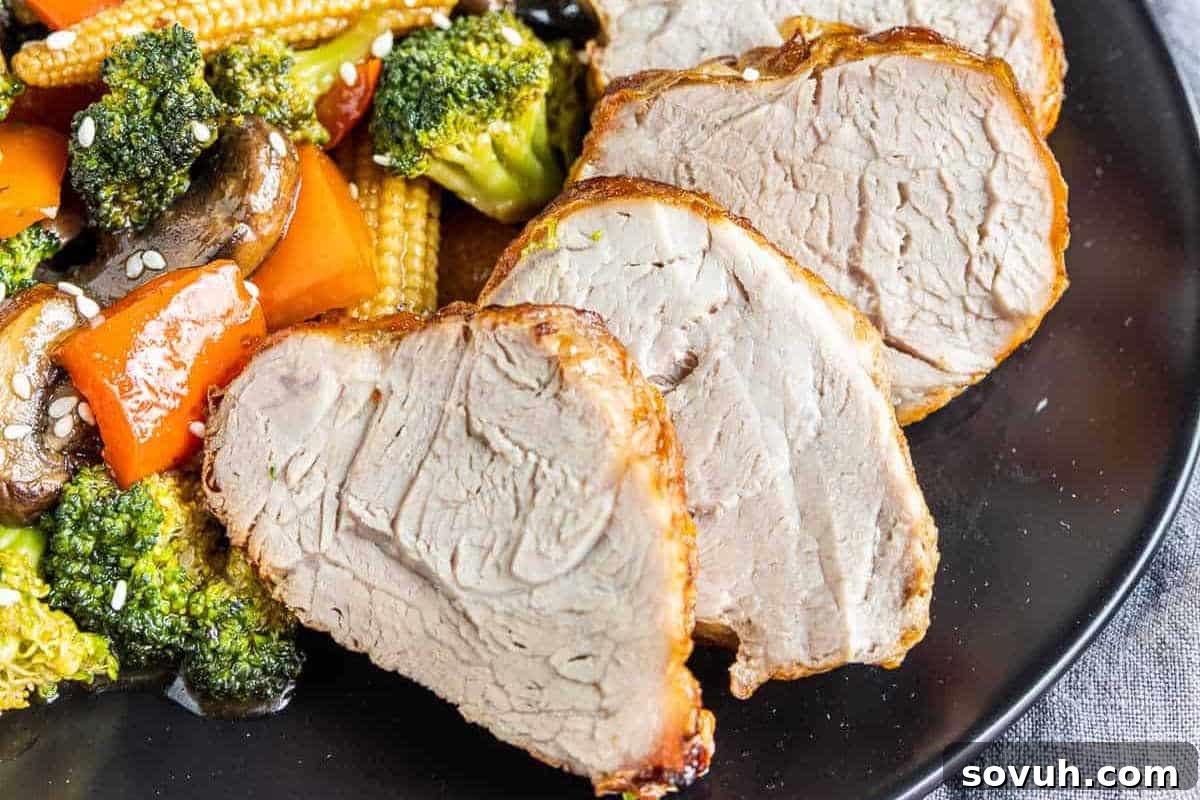 Slices of perfectly roasted pork tenderloin, glistening and moist, served alongside a colorful medley of stir-fried vegetables like broccoli, baby corn, and bell peppers, topped with sesame seeds.