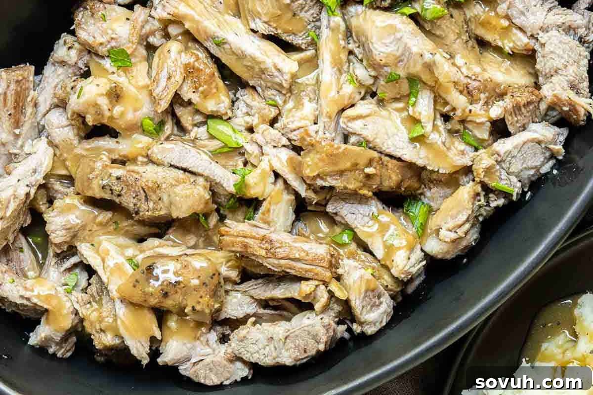 A close-up shot of a platter filled with thick slices of tender, cooked pork roast, richly drizzled with homemade gravy and garnished with fresh herbs. Rice is visible in the background.