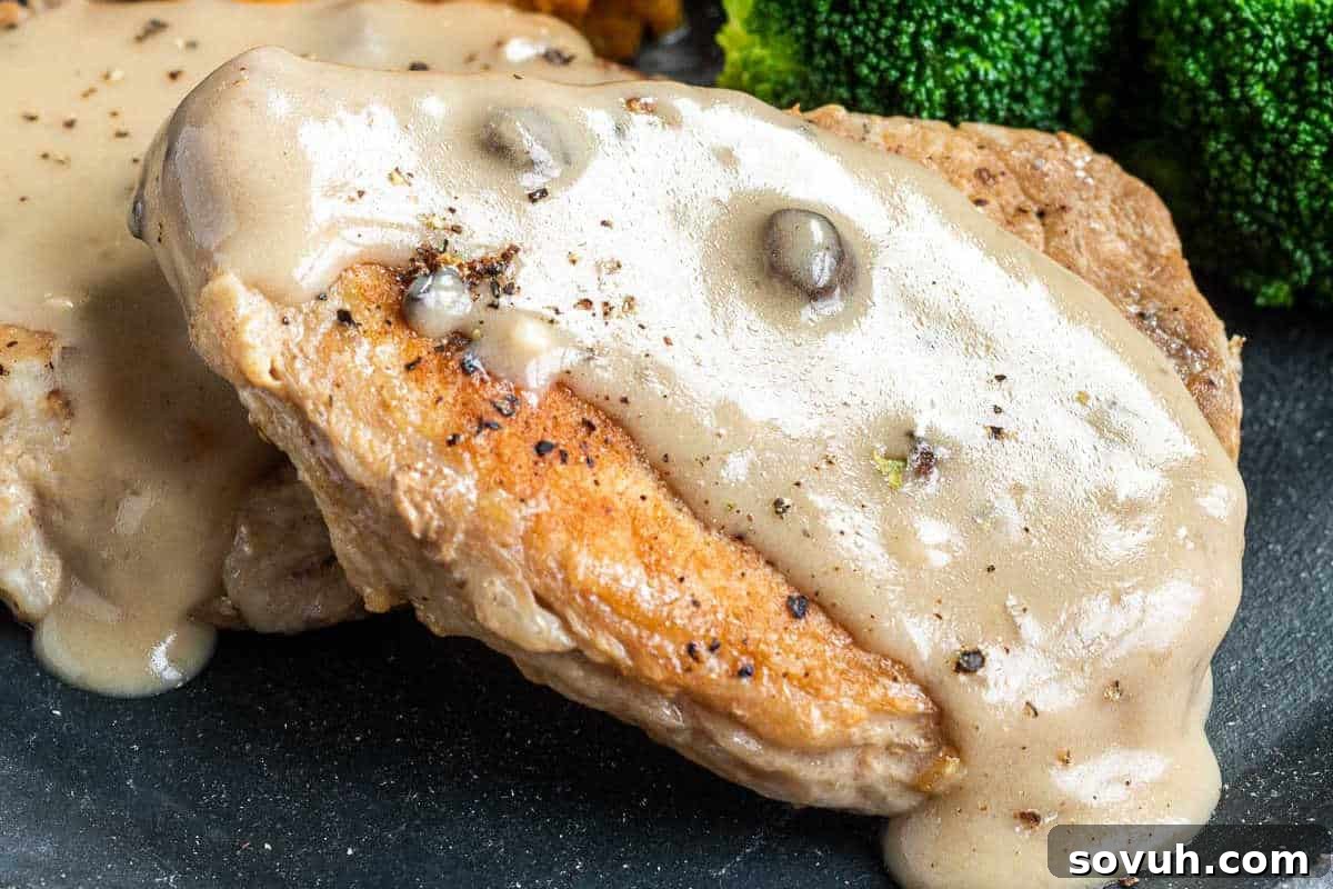 A close-up of a perfectly cooked pork chop generously covered in a rich, creamy mushroom sauce, served on a plate with a side of vibrant green broccoli in the background.