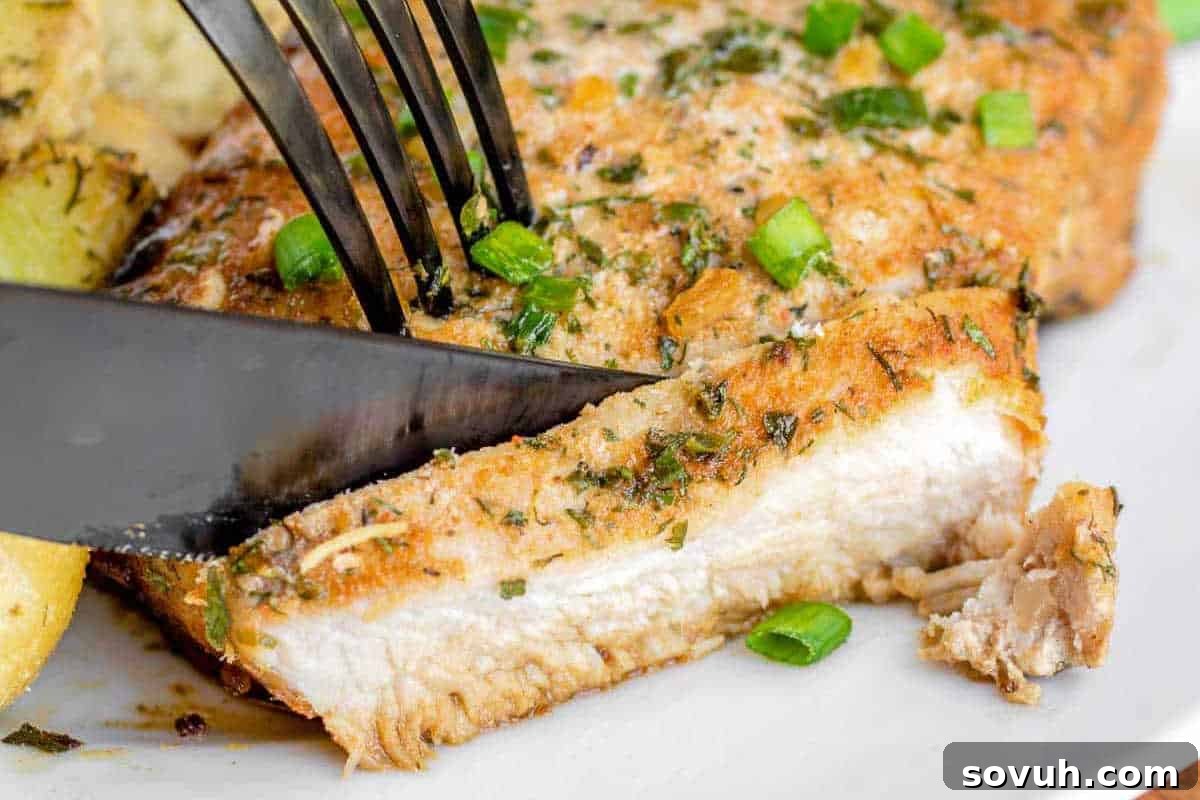 A cooked piece of fish garnished with fresh herbs and green onions is being sliced by a knife and fork on a white plate. Note: The image alt text from the original suggests fish, but this section is about pork chops.