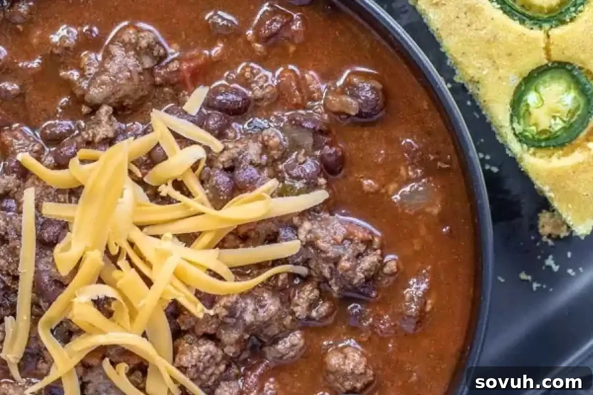 A close-up of a plate with a serving of chili topped with shredded cheese and a piece of jalapeño cornbread on the side.