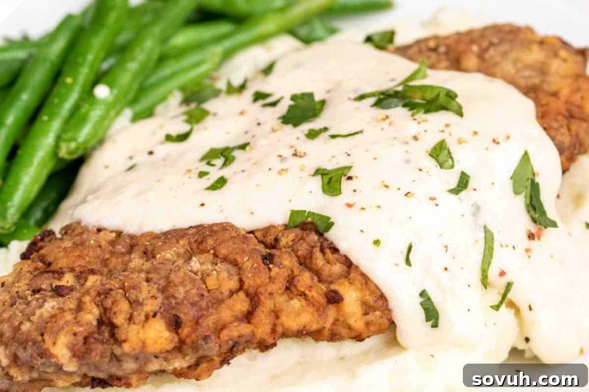 A plate of country fried steak topped with white gravy and garnished with parsley, served with green beans.