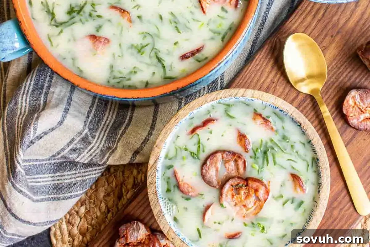 Bowls of creamy soup with herbs and sausage slices, accompanied by a gold spoon on a wooden surface with a striped cloth napkin.
