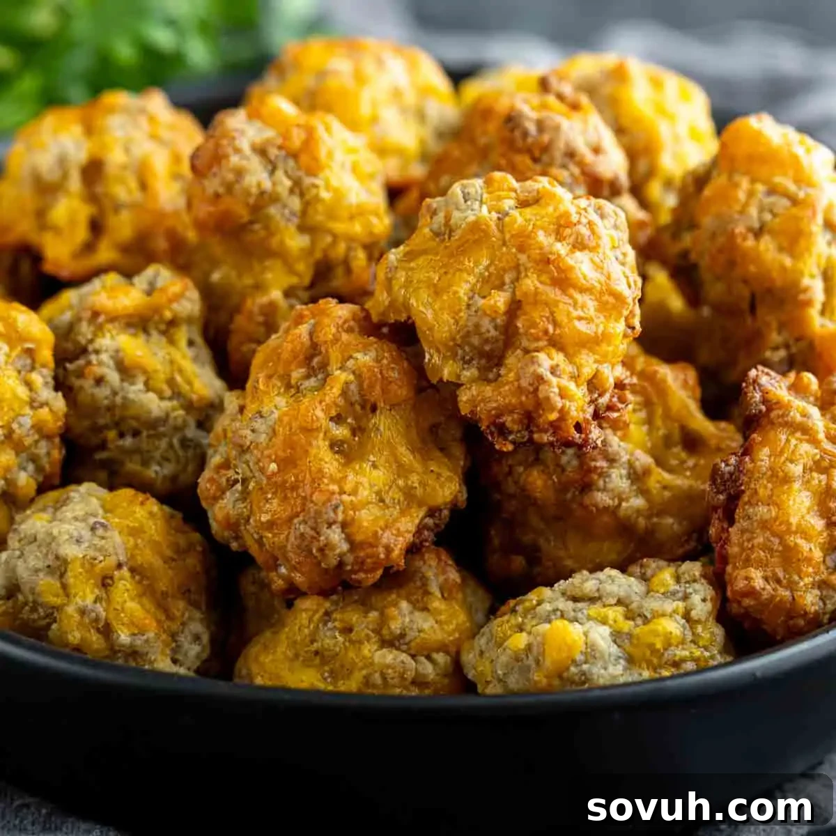 A black bowl filled with baked, golden-brown sausage cheese balls, ready to be served as an appetizer or breakfast item.