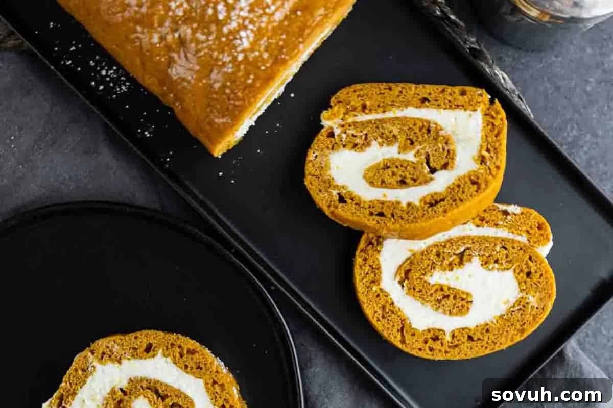 A sliced pumpkin roll cake with cream filling on a black rectangular tray, accompanied by a slice on a black round plate next to it—a perfect centerpiece for your fun fall baking adventures.