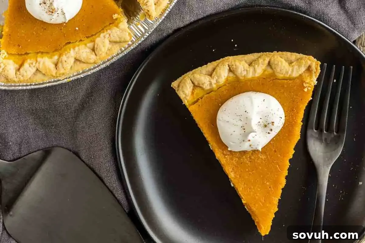 A slice of sweet potato pie with a dollop of whipped cream on a black plate, accompanied by a black fork.