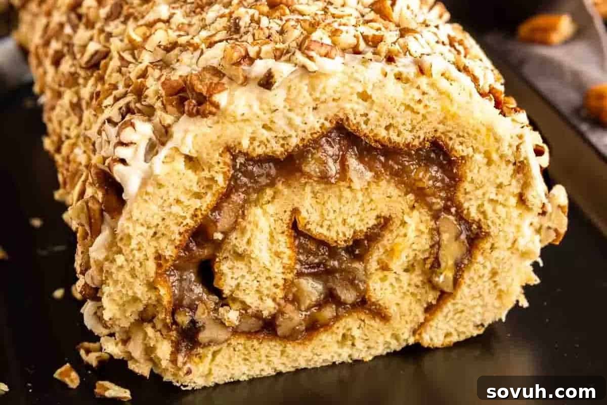 A close-up view of a nut-filled pastry roll sliced through the center, revealing its swirled filling. The roll, a masterpiece of tasty baking, is topped with chopped nuts and placed on a dark surface.