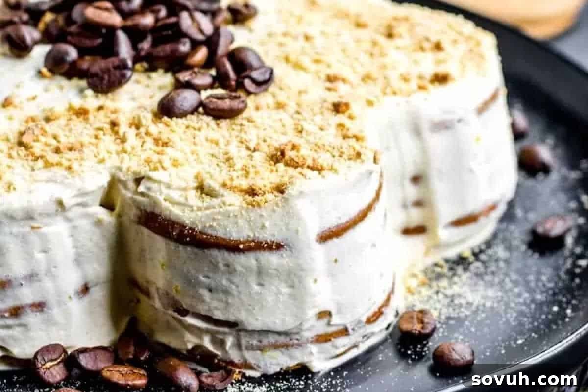 A close-up of a tiramisu cake with layers of cream and coffee-soaked biscuits, topped with coffee beans and a sprinkle of crumbs on a black plate. Perfect for some fun baking, this delightful treat is sure to impress.