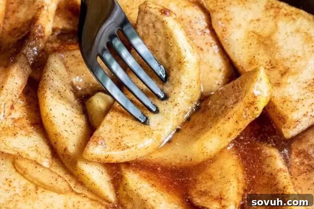 A fork picking up a slice of cooked apple glazed with cinnamon and sugar.