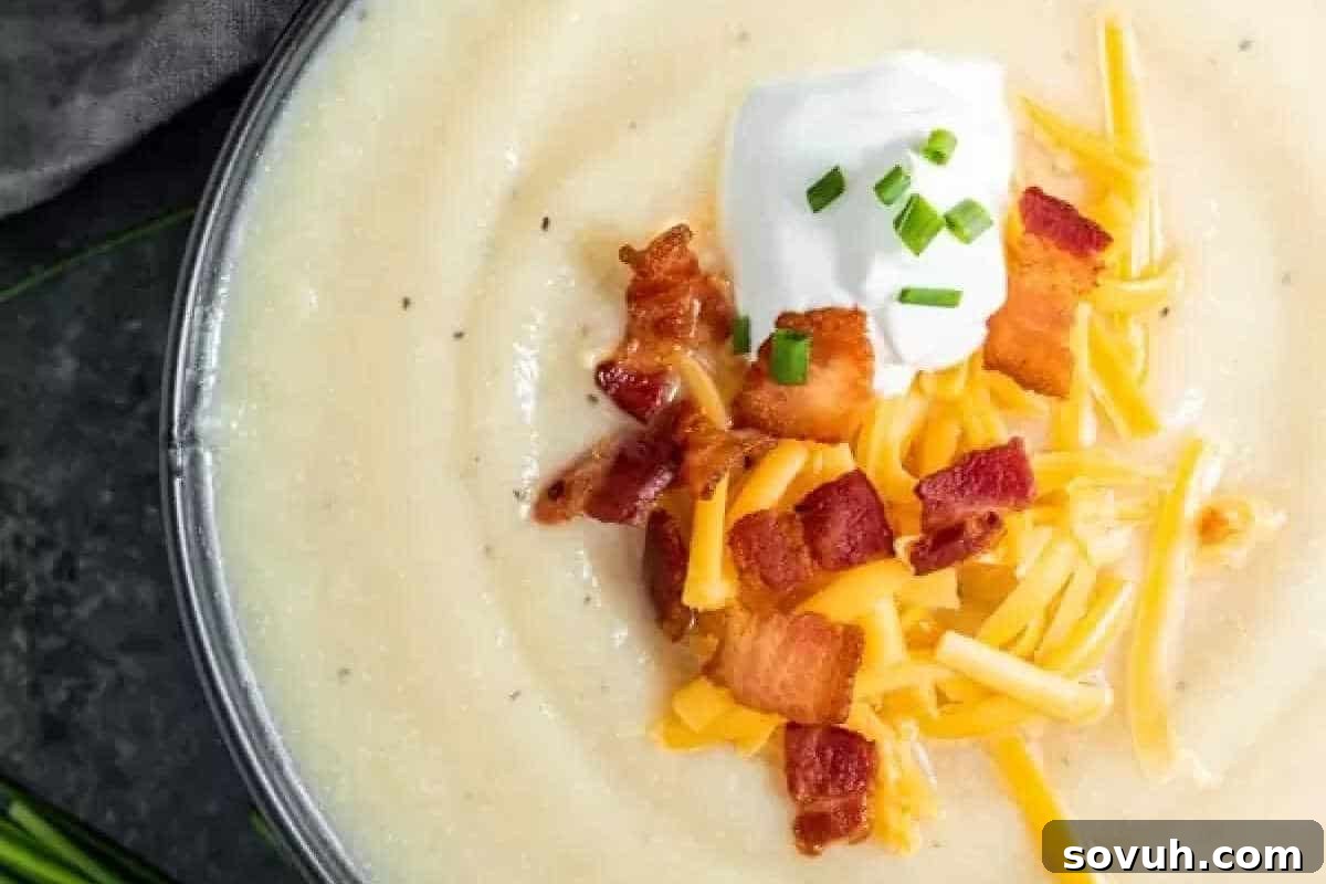 A bowl of creamy potato soup topped with shredded cheese, crispy bacon pieces, a dollop of sour cream, and chopped chives.