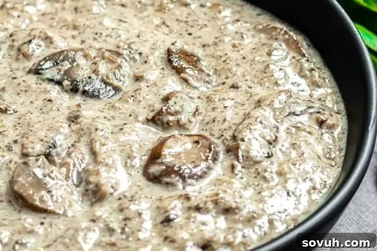 Close-up of a creamy mushroom soup in a black bowl, featuring sliced mushrooms in a thick, speckled broth.
