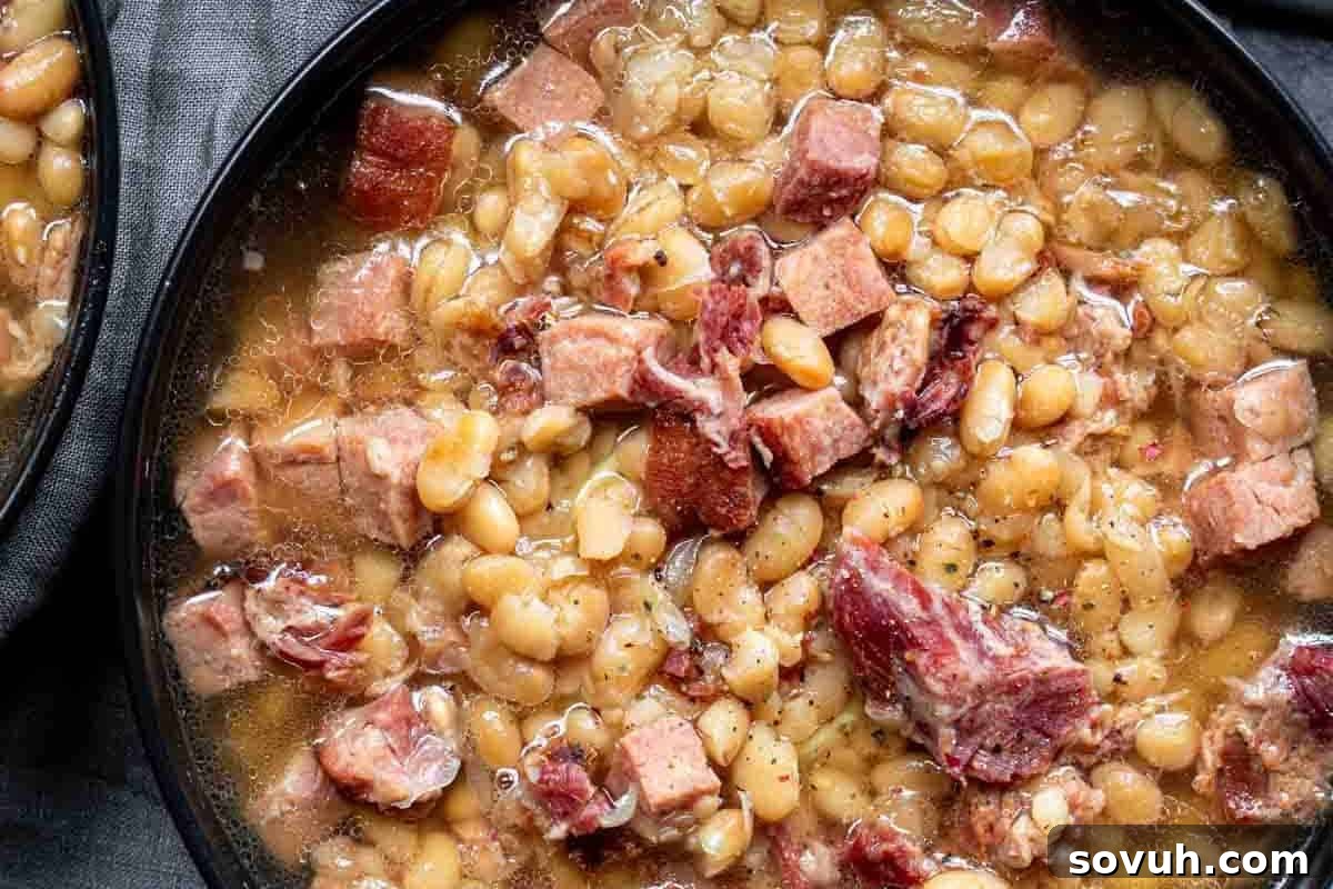 A bowl of white beans cooked with chunks of ham, served in a broth.