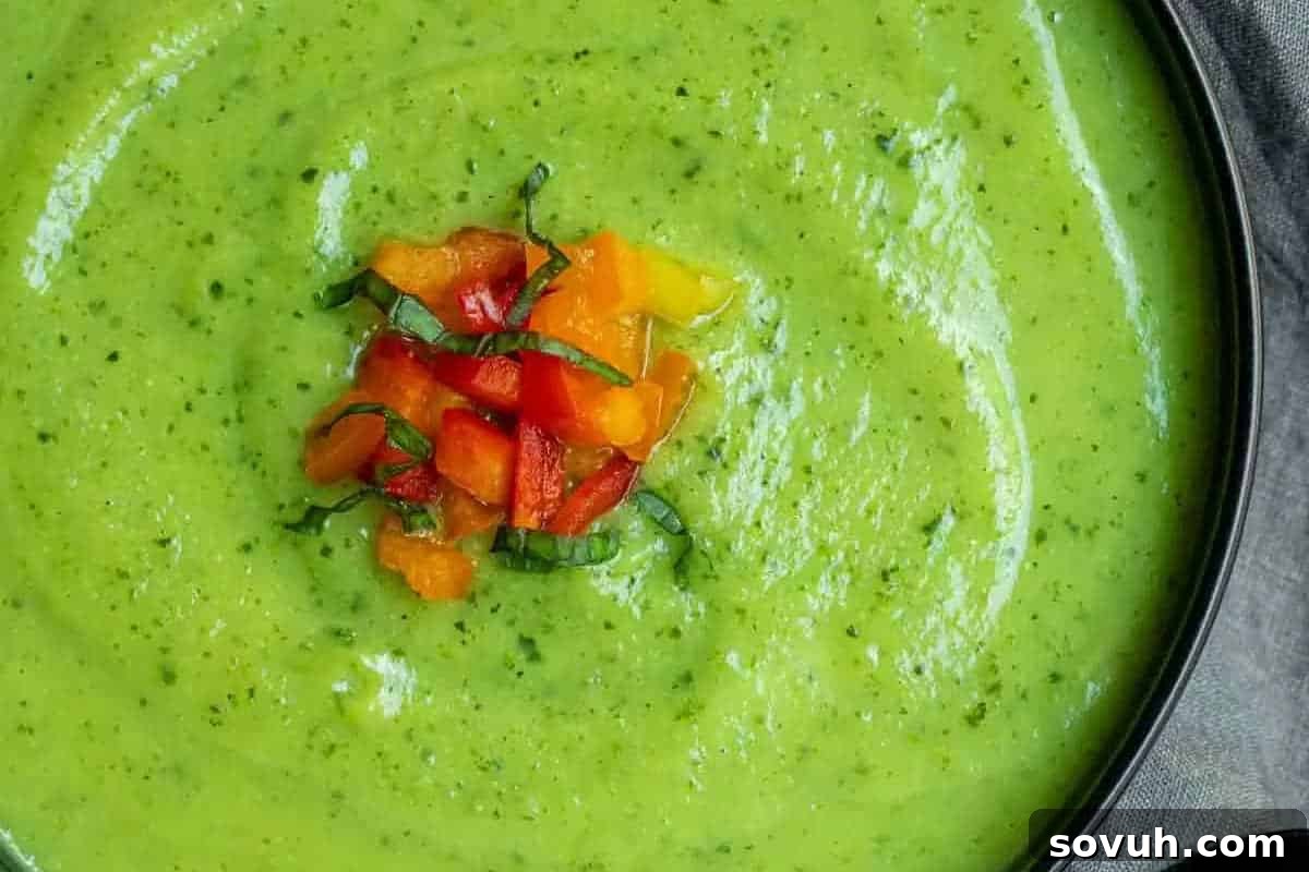 A bowl of creamy green soup garnished with diced red and yellow bell peppers and basil.