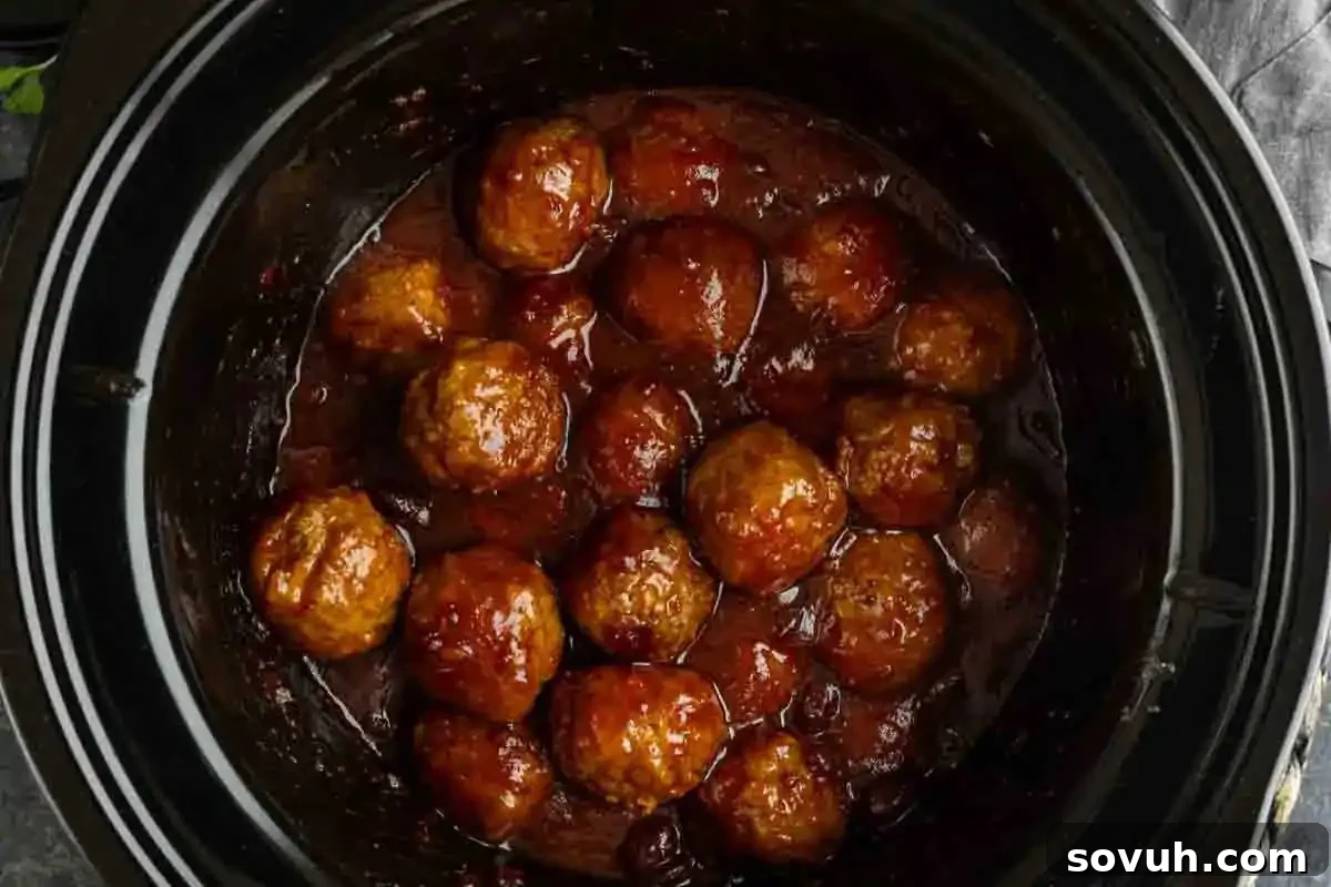 A black slow cooker filled with meatballs coated in a thick, dark sauce.