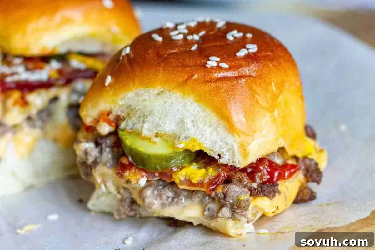 Close-up of a cheeseburger slider with a sesame seed bun, showing cheese, pickles, ketchup, and mustard.
