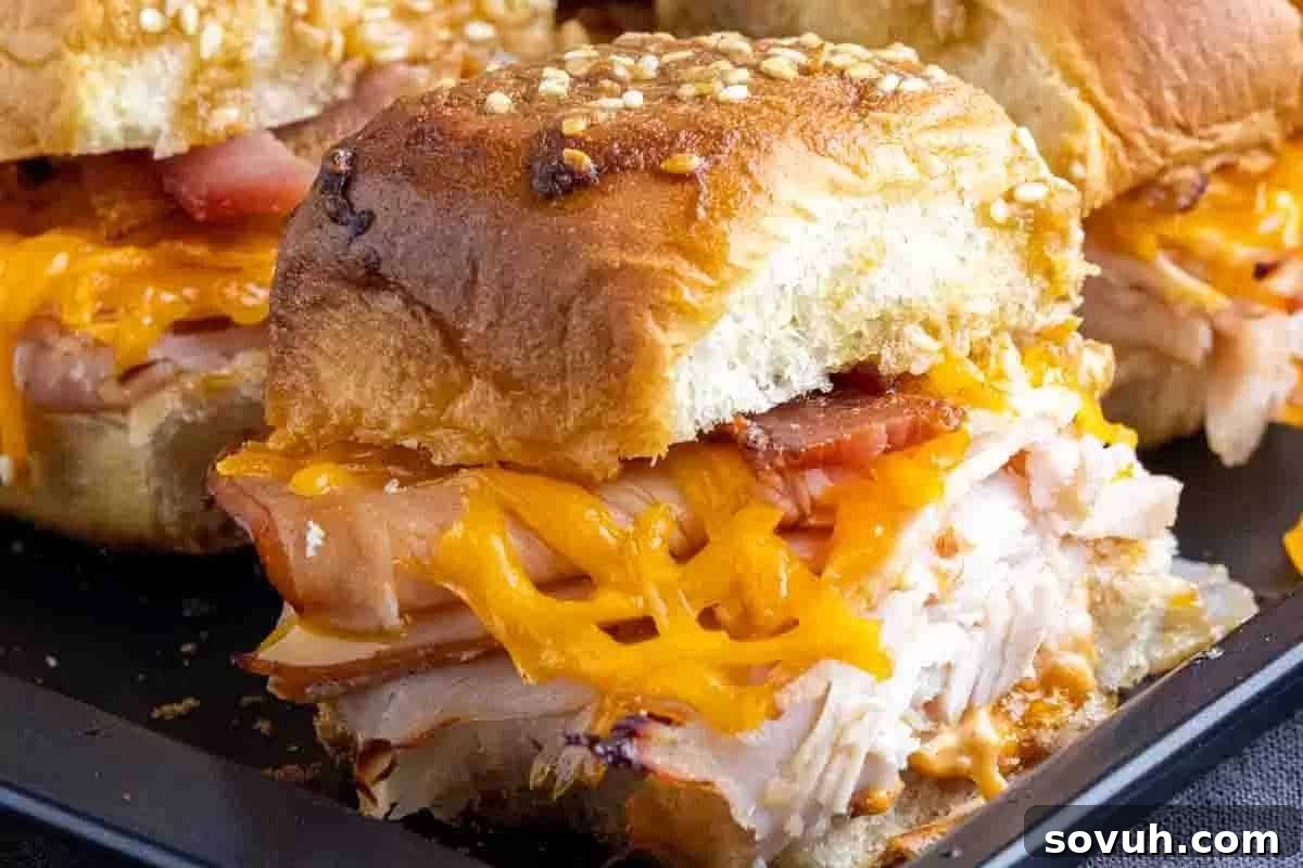 Close-up of a slider sandwich with shredded roasted turkey, melted cheddar cheese, and a slice of tomato on a sesame seed bun.