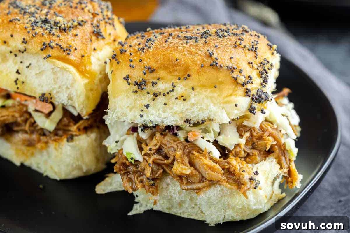 Two BBQ pulled pork sliders with coleslaw and poppy seed-topped buns served on a black plate.
