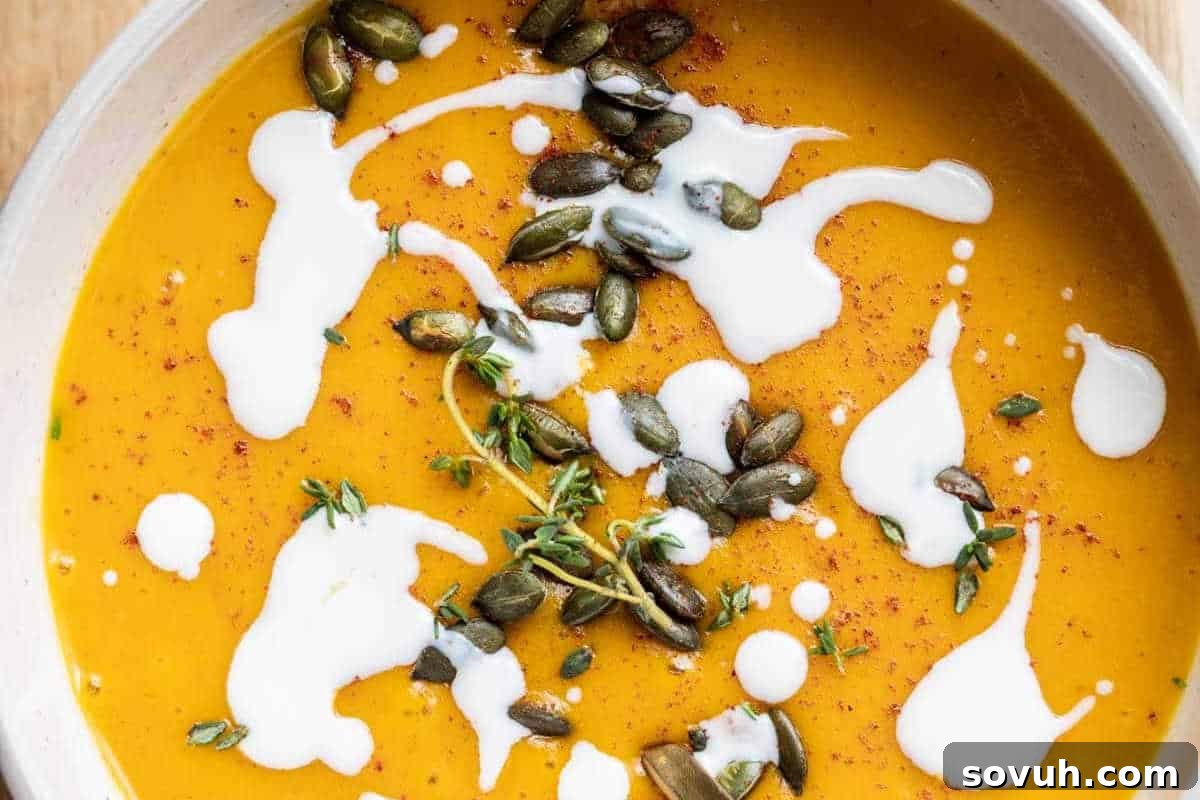 A beautifully presented bowl of creamy pumpkin soup, garnished with crunchy pumpkin seeds, a swirl of white cream, fresh thyme sprigs, and a light sprinkle of seasoning, inviting a comforting autumn meal.