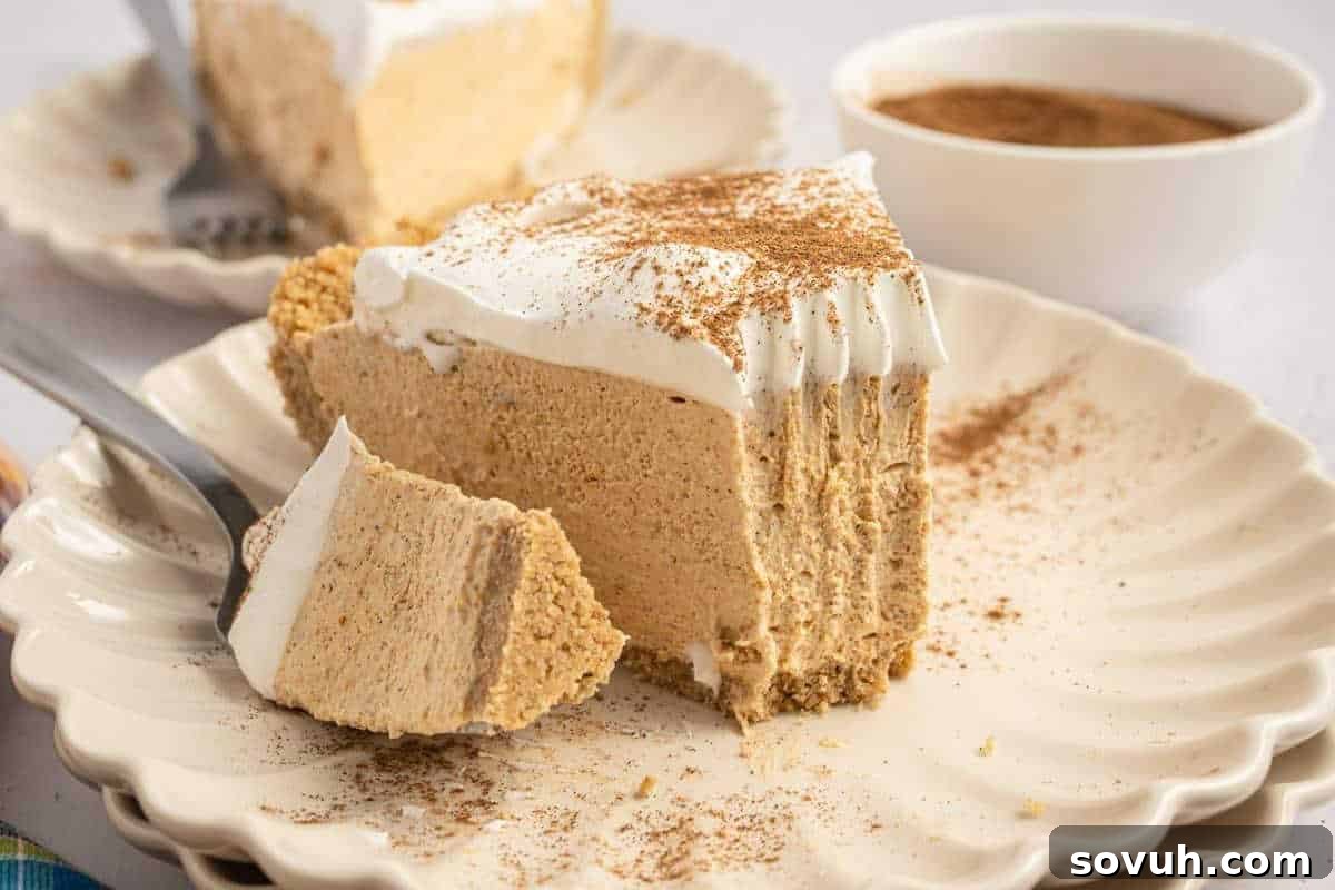 A delectable slice of no-bake pumpkin cream pie, generously topped with a swirl of whipped cream, is artfully presented on a white plate with a fork poised to enjoy. In the softly blurred background, a bowl of cinnamon hints at the warm spices infused in this autumnal dessert.