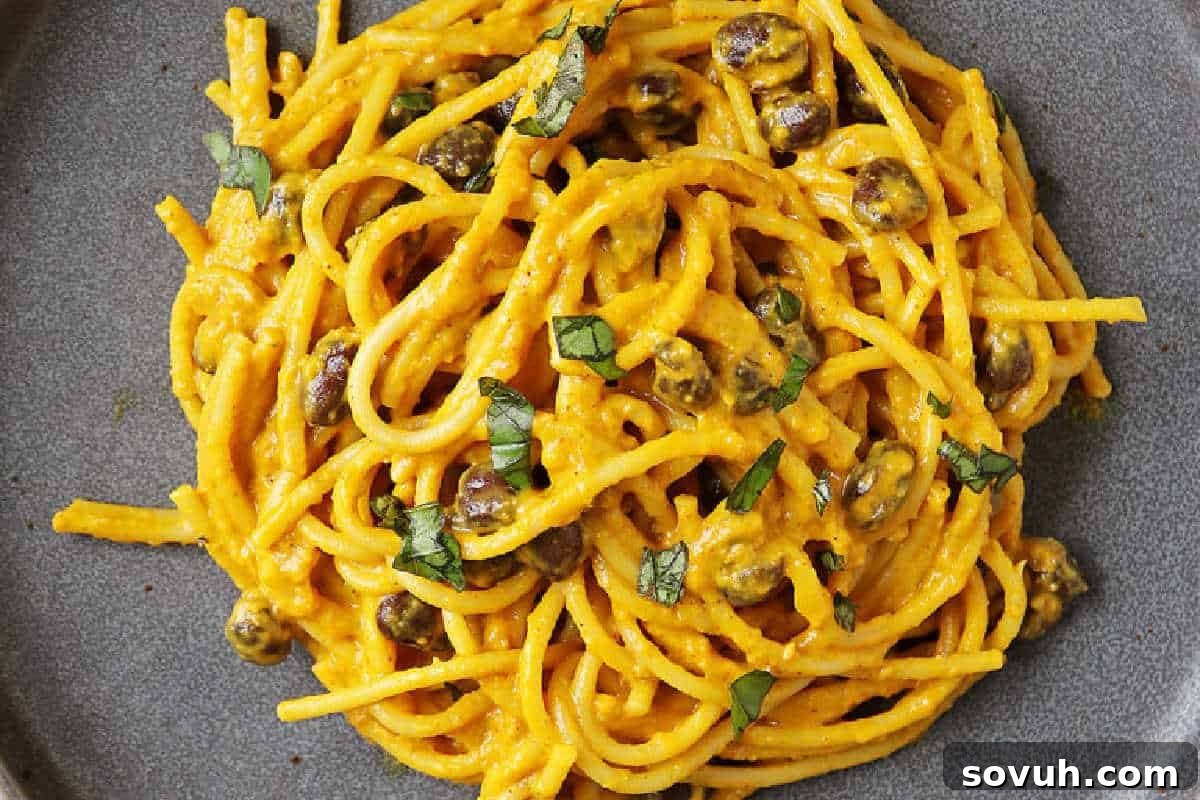 A generously filled plate of spaghetti enveloped in a rich, creamy pumpkin sauce, elegantly garnished with briny capers and a sprinkle of fresh chopped herbs, showcasing a flavorful and easy-to-make vegetarian meal.
