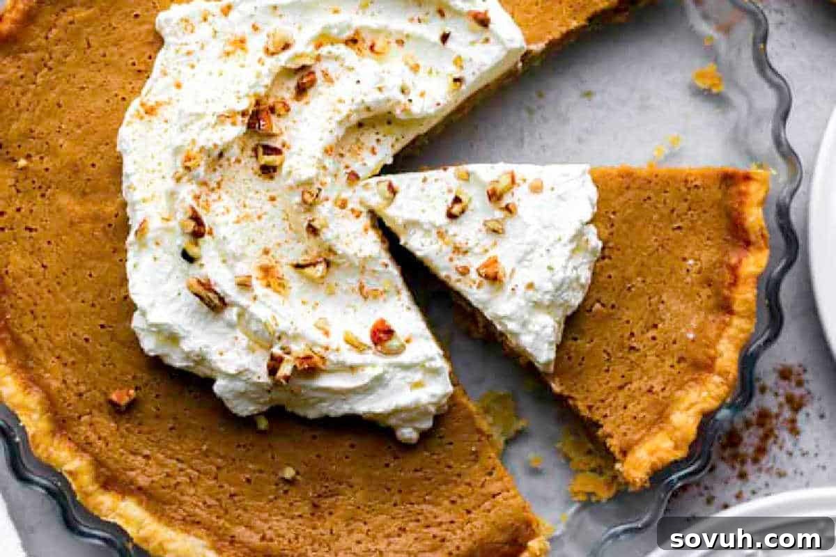 A beautifully baked pumpkin pie, with one slice already removed, elegantly topped with a generous swirl of whipped cream and a sprinkle of chopped nuts. The pie sits invitingly, showcasing its golden crust and creamy filling, hinting at its delicious flavor.