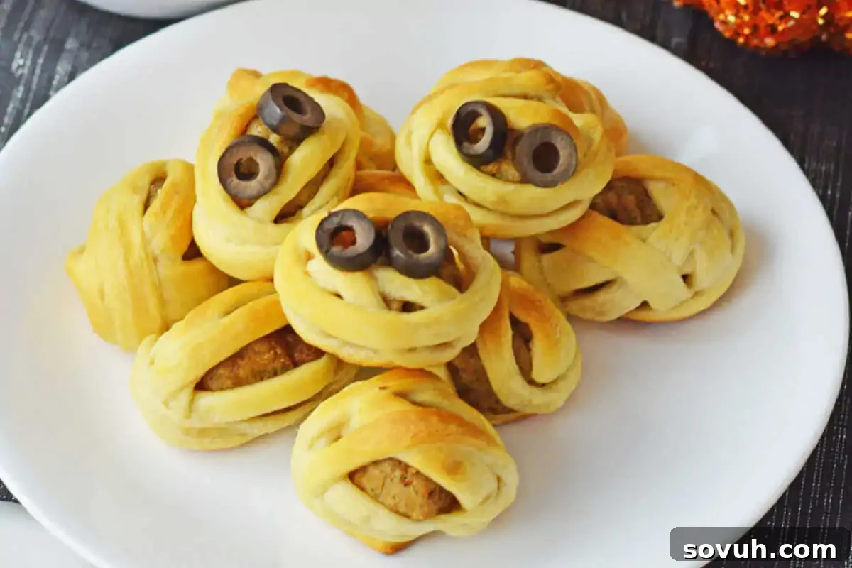 A plate of baked mummy-themed snacks, wrapped in pastry with black olive slices for eyes.