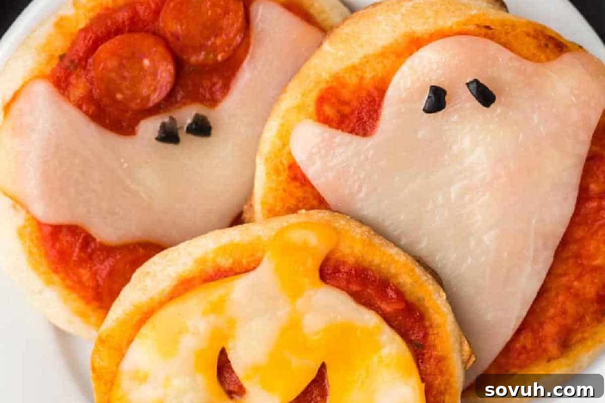 Three mini pizzas topped with ghost and pumpkin shapes made of cheese and pepperoni.