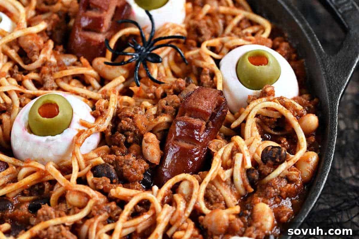 Spaghetti with ground meat, topped with fake rubber spiders, eggs resembling eyes with olives and peppers, and sausage fingers in a pan.