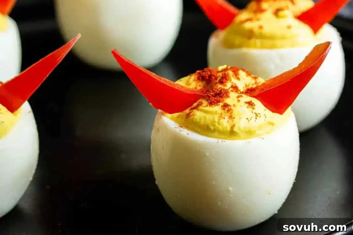 Deviled eggs garnished with red pepper slices and a sprinkle of paprika on a black plate.