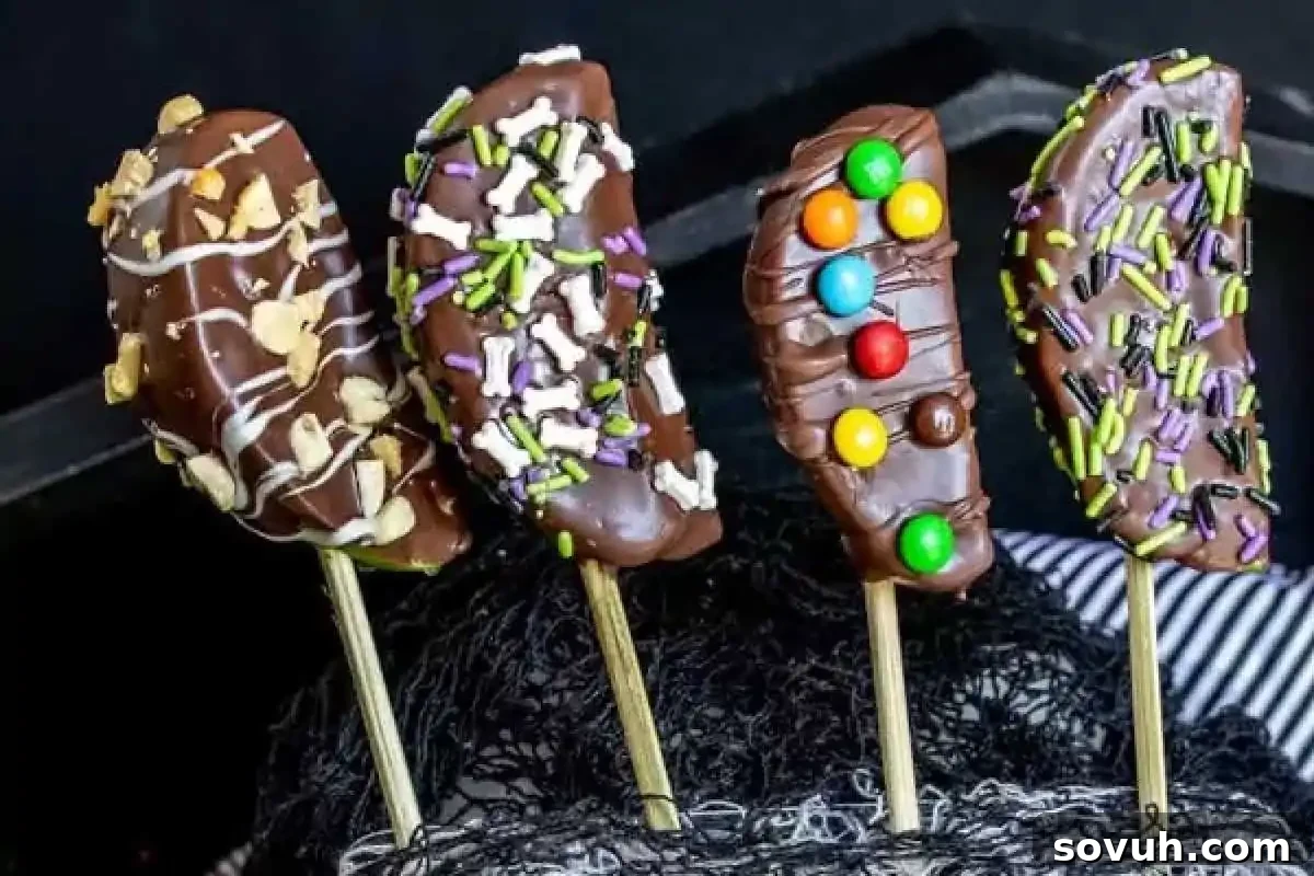 Four chocolate-dipped banana pops with assorted toppings including sprinkles, nuts, and colorful candies, on wooden sticks.