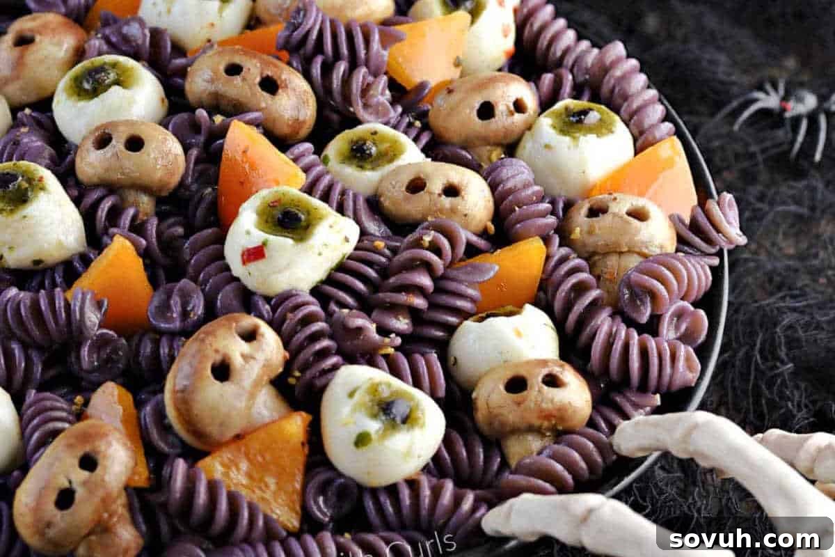 A plate of purple pasta with orange bell peppers, mushrooms resembling eyeballs, and white mini mozzarella balls. Skeleton fingers in the foreground and a spider in the background.