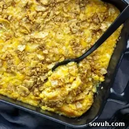A baked casserole with a crispy cracker topping in a black dish, partially served with a spoon.