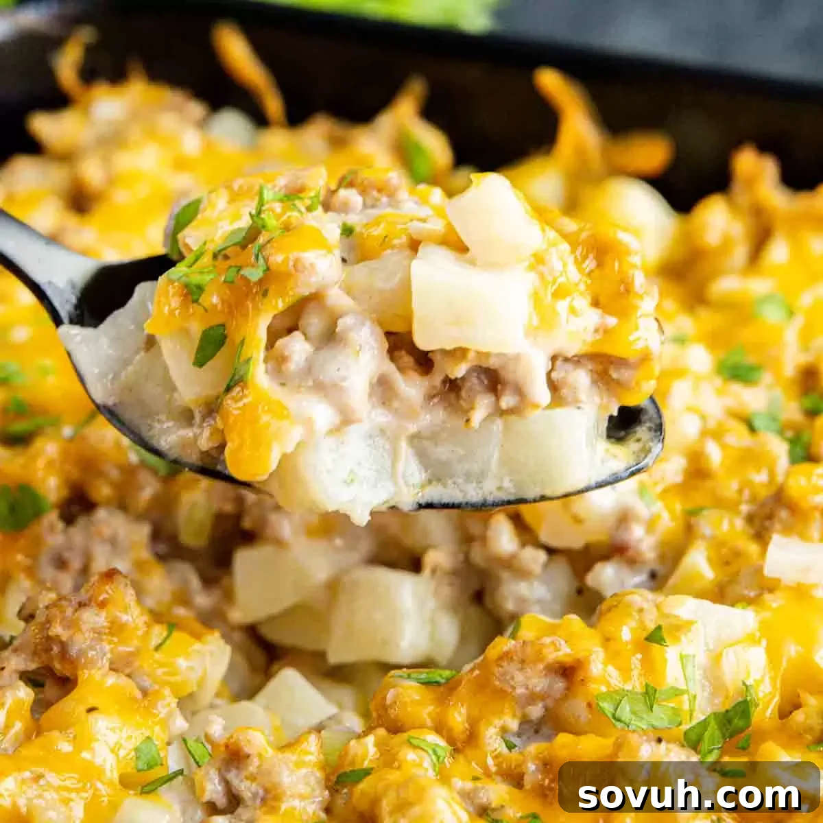 A generous spoonful of golden-brown cheesy Sausage Potato Casserole being lifted from a baking dish.