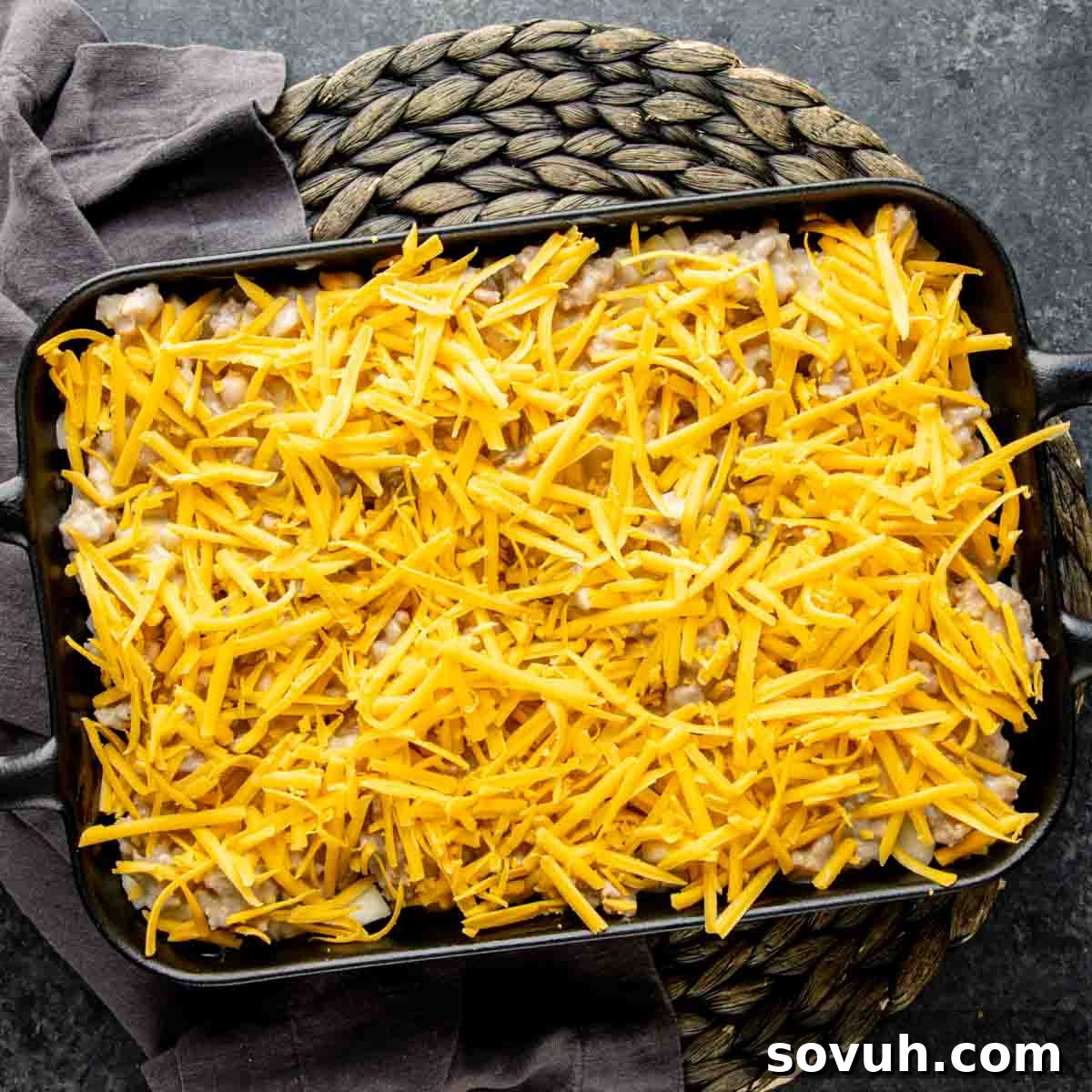 A fully assembled cheesy Sausage Potato Casserole in a sleek black baking dish, covered with foil, ready for baking.